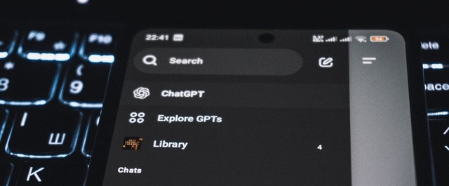 Tela de smartphone com menu do ChatGPT exibindo opções como 'Explore GPTs', 'Library', 'Chats' e histórico de conversas recentes, com teclado iluminado em background.